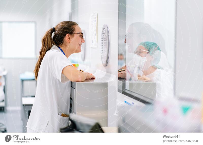Lächelnde Ärztin im Gespräch mit Mitarbeiterin durch Fenster in der Apotheke Farbaufnahme Farbe Farbfoto Farbphoto Spanien Innenaufnahme Innenaufnahmen innen