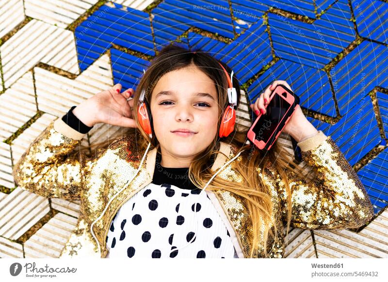 Porträt eines Mädchens mit goldener Paillettenjacke, das mit Kopfhörern und Smartphone Musik hört Jacke Jacken Kopfhoerer Portrait Porträts Portraits iPhone