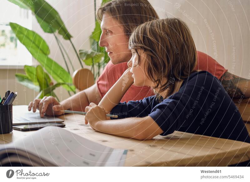 Vater und Sohn benutzen Laptop, während sie zu Hause Hausaufgaben machen Farbaufnahme Farbe Farbfoto Farbphoto Innenaufnahme Innenaufnahmen innen drinnen Tag