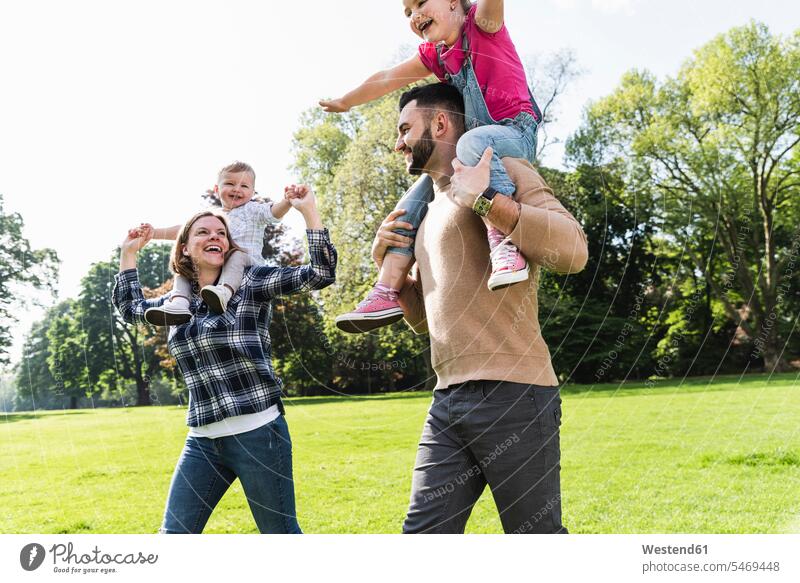 Glückliche Eltern tragen Kinder auf den Schultern in einem Park Familie Familien Huckepack transportieren Parkanlagen Parks glücklich glücklich sein