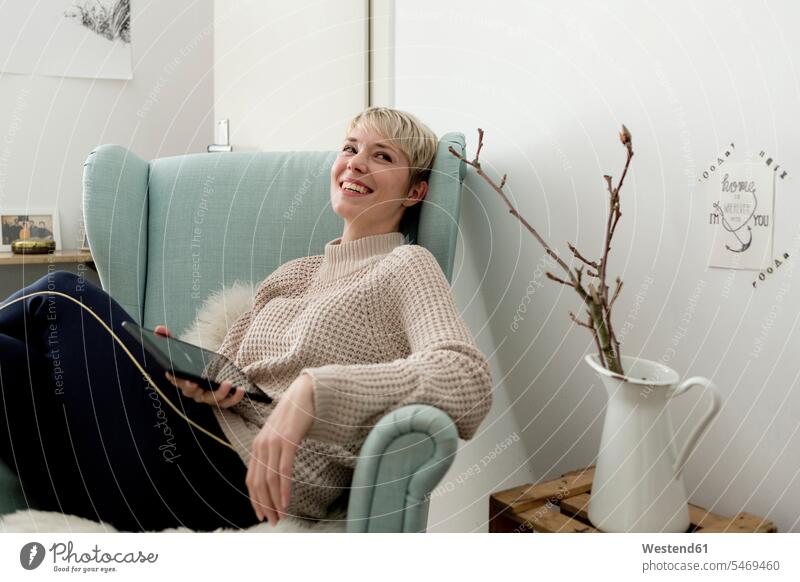 Glückliche Frau sitzt im Sessel zu Hause mit Tablet Deutschland ausruhen Rast Erholung erholen Wohnung wohnen Wohnungen Krug Krüge Kruege offenes Lächeln lachen