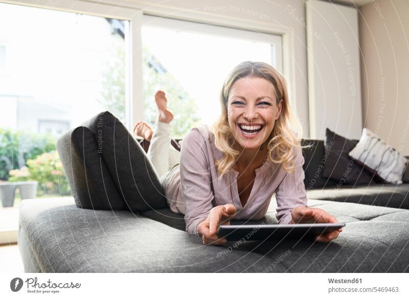 Porträt einer lachenden Frau, die zu Hause auf einer Couch liegt und ein Tablett benutzt liegen liegend Portrait Porträts Portraits Tablet Computer Tablet-PC
