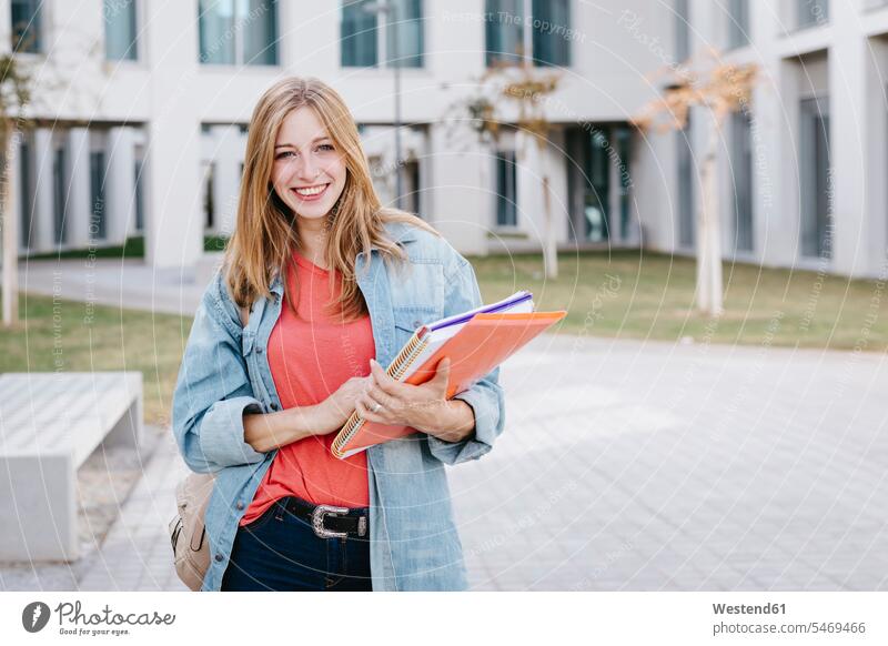 Lächelnde schöne blonde junge Frau hält Bücher auf dem Universitätscampus schöne Frau schöne Frauen Mensch Menschen Leute People Personen Campus