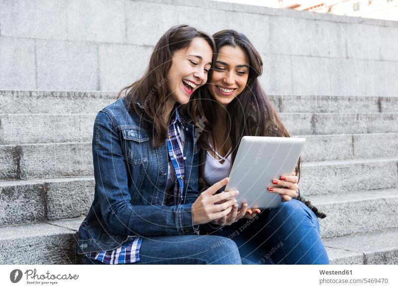 Glückliche junge Frauen beobachten Tablette sitzen auf Stufen zusammen in Madrid, Spanien Leute Menschen People Person Personen Europäisch Kaukasier kaukasisch