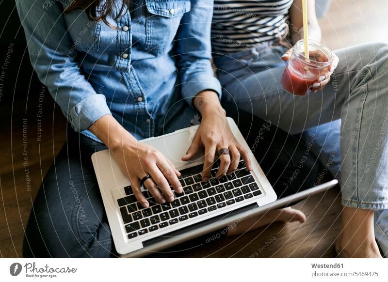 Nahaufnahme von zwei jungen Frauen, die mit Softdrink und Laptop auf dem Boden sitzen weiblich sitzend sitzt Erfrischungsgetränk Erfrischungsgetraenk