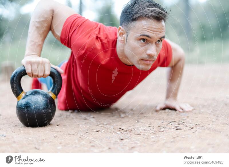 Junger athletischer Mann mit Hantel in den Wäldern T-Shirts rote roter rotes Muße Anreiz Ansporn Antrieb motivieren motiviert trainieren Forst außen draußen