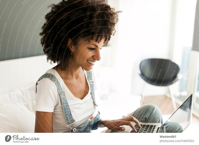 Lächelnde Frau sitzt auf dem Bett und benutzt einen Laptop weiblich Frauen Betten Notebook Laptops Notebooks lächeln sitzen sitzend Erwachsener erwachsen Mensch