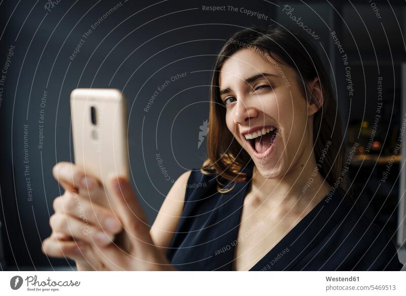 Porträt einer jungen Frau mit Smartphone, die lustige Gesichter zieht Kleider Telekommunikation Handies Handys Mobiltelefon Mobiltelefone Gesichtsausdruck