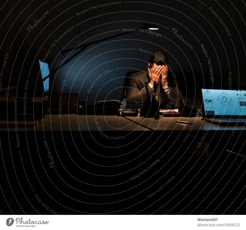 Überbeanspruchter Geschäftsmann sitzt im Dunkeln an seinem Schreibtisch Büro Office Büros sitzen sitzend Arbeitstisch Schreibtische Nacht nachts Überlastung