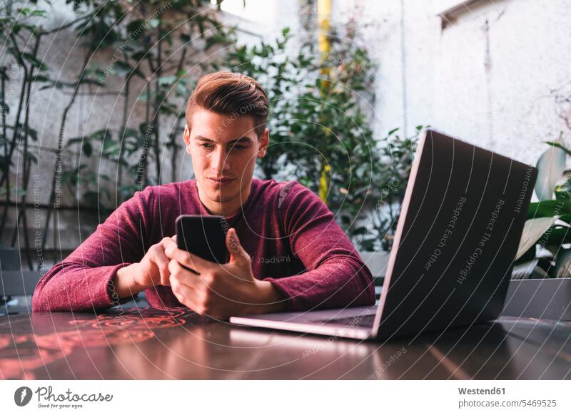 Junger Mann sitzt am Tisch und benutzt Handy und Laptop Italien chatten Chat Selbstständigkeit Selbständigkeit Freiberufler Smartphone iPhone Smartphones