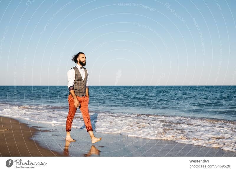 Gut gekleideter Mann, der an einem Strand am Wasser spazieren geht Leute Menschen People Person Personen Europäisch Kaukasier kaukasisch 1 Ein ein Mensch
