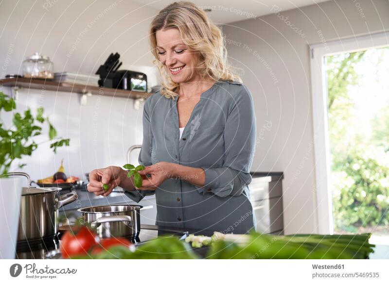 Lächelnde Frau kocht in Küche und legt Basilikum in Kochtopf lächeln kochen Kochtöpfe Kochtoepfe Topf Töpfe weiblich Frauen Küchen Küchenkraut Kuechenkraeuter