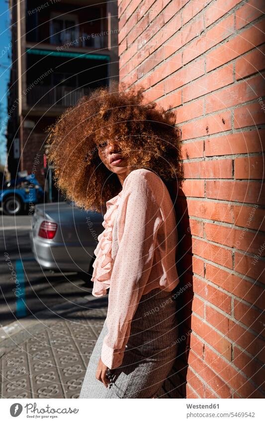 Porträt einer schönen jungen Frau mit Afro-Frisur, die an einer Ziegelmauer in der Stadt lehnt staedtisch städtisch weiblich Frauen Afrolook Afros Afro-look
