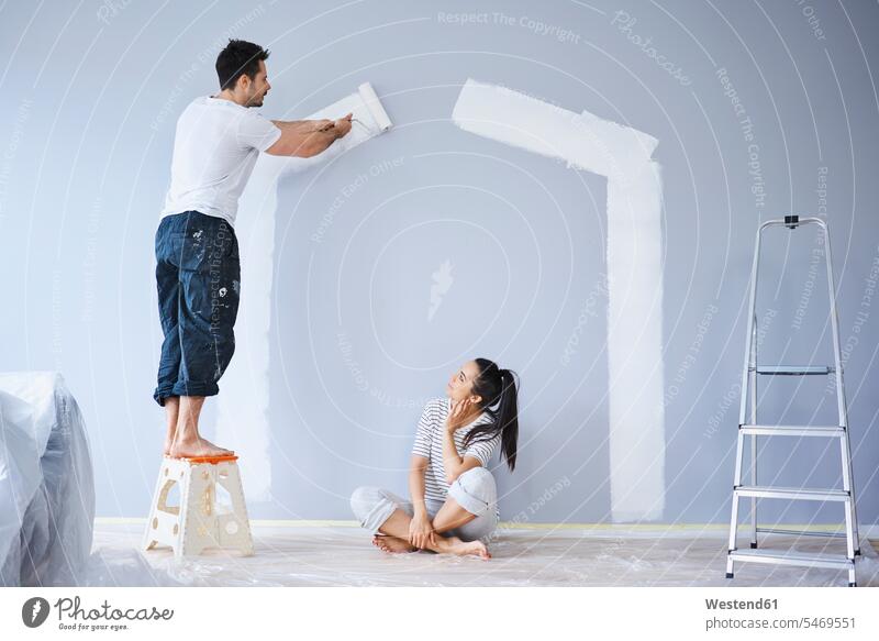 Ehepaar streicht Hausform an Wand in neuer Wohnung wohnen Wohnungen Häuser Haeuser streichen Paar Pärchen Paare Partnerschaft Form Formen Wände Waende Wohnen