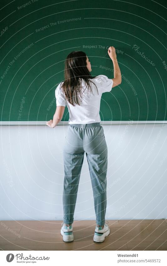 Rückansicht in voller Länge einer jungen Studentin, die an einer Tafel im Klassenzimmer der Universität schreibt Farbaufnahme Farbe Farbfoto Farbphoto