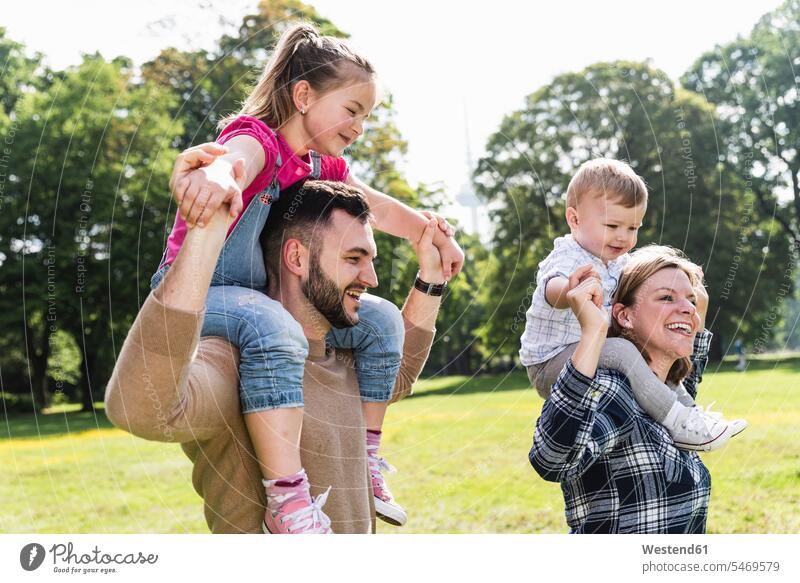 Glückliche Eltern tragen Kinder auf den Schultern in einem Park transportieren Familie Familien glücklich glücklich sein glücklichsein Parkanlagen Parks