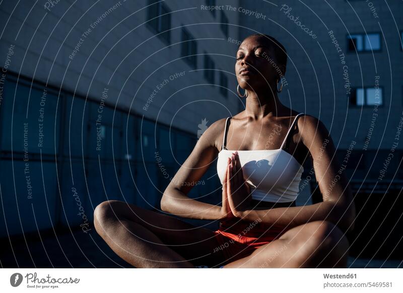Junge Frau mit geschlossenen Augen meditiert, während sie gegen ein Gebäude in der Stadt sitzt Farbaufnahme Farbe Farbfoto Farbphoto Freizeitbeschäftigung Muße