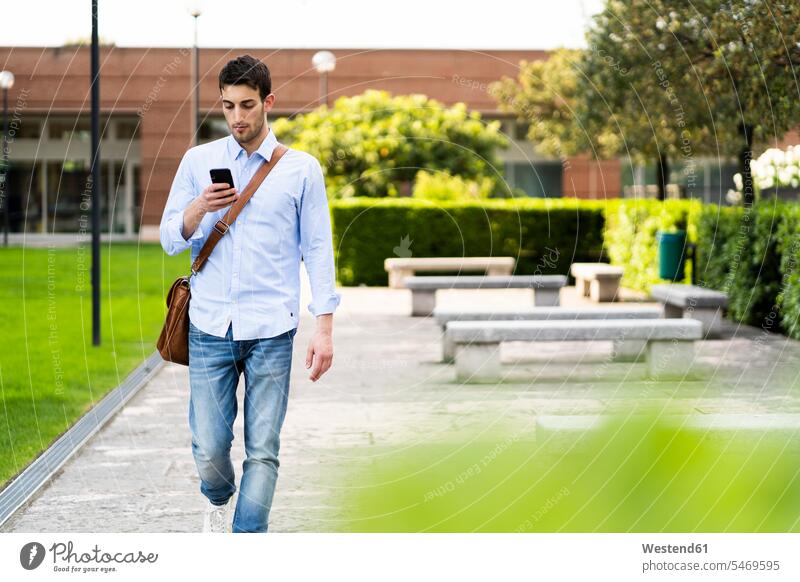 Junger Mann benutzt Smartphone in der Stadt Hemden Bänke Sitzbank Sitzbänke Telekommunikation telefonieren Handies Handys Mobiltelefon Mobiltelefone Arbeit