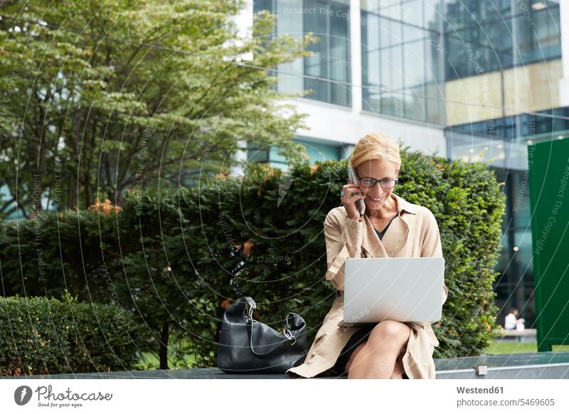 Geschäftsfrau telefoniert mit dem Handy, während sie im Büropark am Laptop arbeitet Farbaufnahme Farbe Farbfoto Farbphoto Außenaufnahme außen draußen im Freien