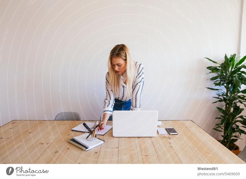 Junge Geschäftsfrau am Schreibtisch stehend, mit Laptop steht Laptop benutzen Laptop benützen Arbeitstisch Schreibtische blond blonde Haare blondes Haar