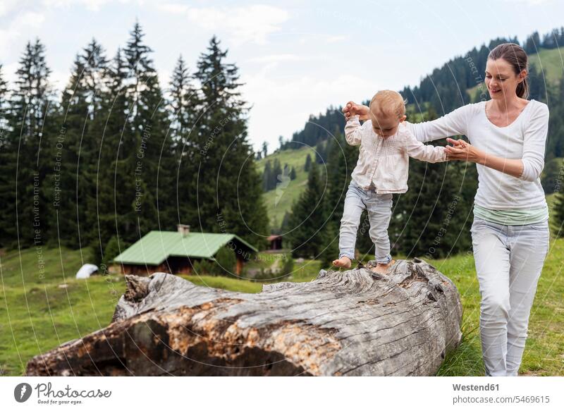 Deutschland, Bayern, Oberstdorf, Mutter hilft kleiner Tochter beim Balancieren auf einem Baumstamm helfen mithelfen Hilfsbereitschaft beistehen Mithilfe