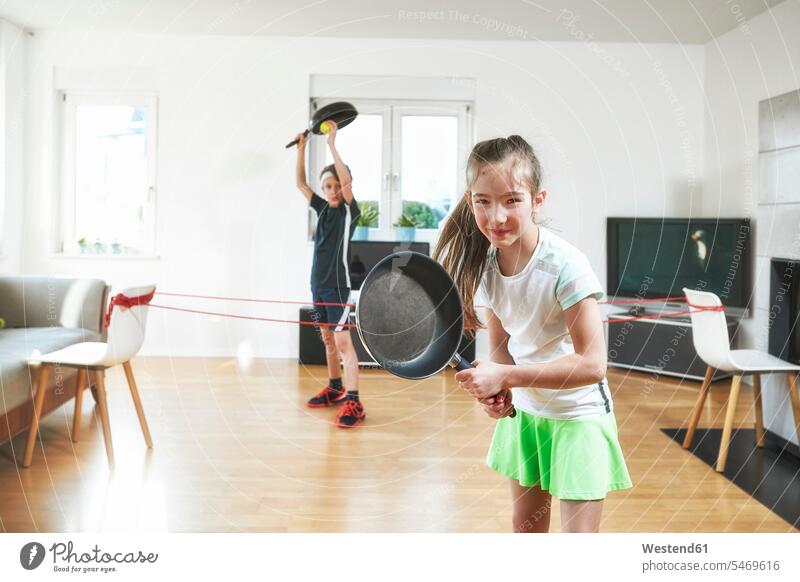 Lächelnde Schwester spielt Tennis mit Bruder zu Hause in Quarantäne Farbaufnahme Farbe Farbfoto Farbphoto Innenaufnahme Innenaufnahmen innen drinnen Tag