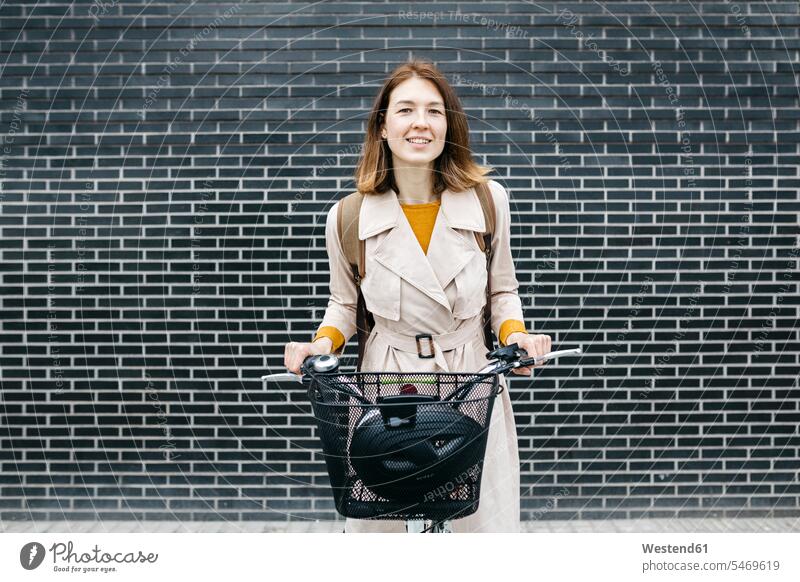Porträt einer lächelnden Frau mit E-Bike an einer Backsteinmauer Portrait Porträts Portraits Fahrrad Bikes Fahrräder Räder Rad Backsteinwand Backsteinmauern