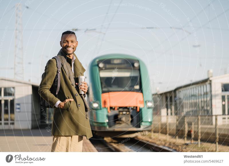 Porträt eines lächelnden Mannes mit wiederverwendbarem Becher, der auf den Zug wartet geschäftlich Geschäftsleben Geschäftswelt Geschäftsperson