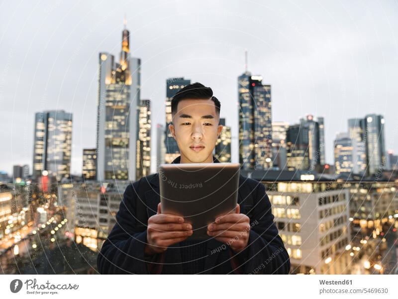Mann benutzt Tablette vor der städtischen Skyline in der Abenddämmerung, Frankfurt, Deutschland Leute Menschen People Person Personen Asiaten Asiatisch