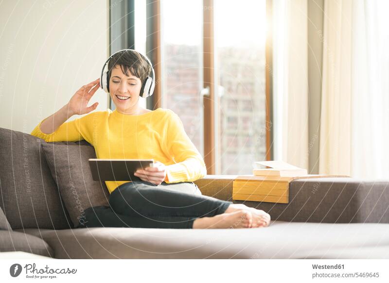Porträt der glücklichen Frau sitzt auf der Couch zu Hause hören Musik mit Kopfhörern, während auf Tablette suchen sitzen sitzend Portrait Porträts Portraits