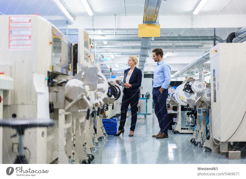 Männlicher Techniker steht in der Nähe einer Geschäftsfrau, die Maschinen in der Fabrik analysiert Farbaufnahme Farbe Farbfoto Farbphoto Innenaufnahme