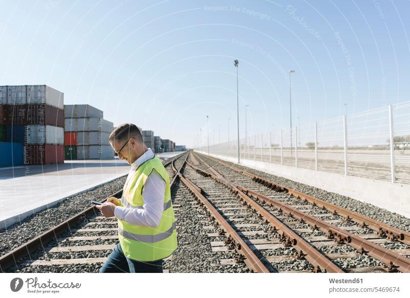 Mann auf Bahngleisen vor Frachtcontainern mit Mobiltelefon Spanien Manager Import weißes Hemd Verbindung verbunden verbinden Anschluss Blick nach unten benutzen