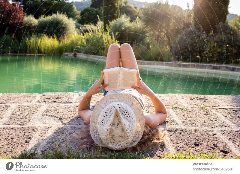 Mädchen mit Strohhut liegt am Schwimmbad und liest ein Buch Bücher entspannen relaxen Lektüre entspanntheit relaxt geniessen Genuss frei Muße auf Achse