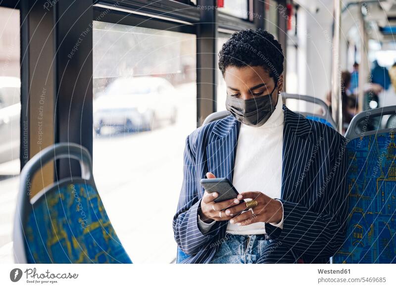 Junge Geschäftsfrau benutzt Mobiltelefon im Bus während COVID-19 Farbaufnahme Farbe Farbfoto Farbphoto Fahrzeuginnenraum Tag Tageslichtaufnahme
