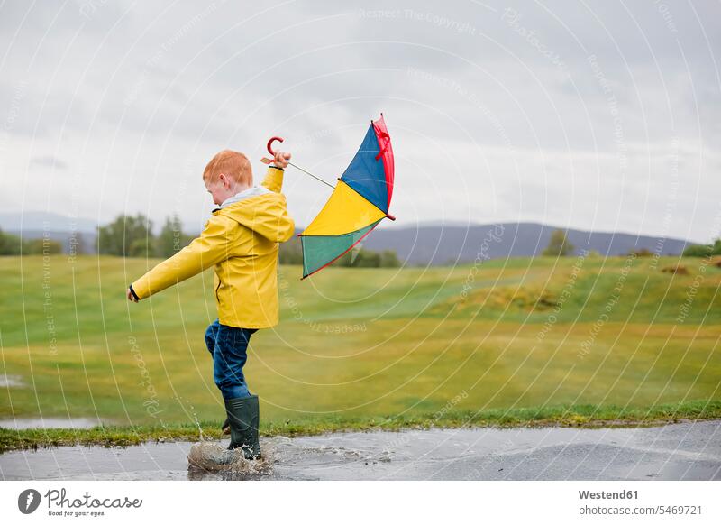 Rothaariger kleiner Junge mit Regenschirm spielt im Regen Buben Knabe Jungen Knaben männlich rothaarig rote Haare rothaarige rotes Haar rothaariger rothaariges