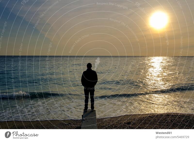 Italien, Ligurien, Riviera di Ponente, Noli, Mann steht bei Sonnenaufgang am Strand Männer männlich Meer Meere Fernweh Reiselust stehen stehend Einsamkeit