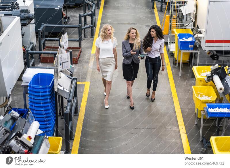 Drei Frauen mit Tablette zu Fuß und im Gespräch in der Fabrik Fabrikhalle sprechen reden Industriehallen Fabrikhallen gehen gehend geht Fabriken weiblich