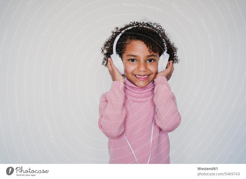 Porträt eines lächelnden kleinen Mädchens mit rosa Rollkragenpullover, das mit Kopfhörern Musik hört Leute Menschen People Person Personen 1 Ein ein Mensch