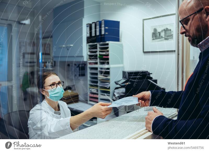 Angestellter am Empfangsschalter der Krankenhausstation übergibt Maske an Besucher Gesundheit Gesundheitswesen medizinisch Erkrankung Erkrankungen Krankheiten