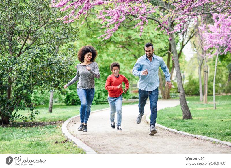 Glückliche Familie läuft und spielt in einem Park Spanien Junge Buben Knabe Jungen Knaben männlich Quality Time Gehweg Weg Kindheit offenes Lächeln lachen
