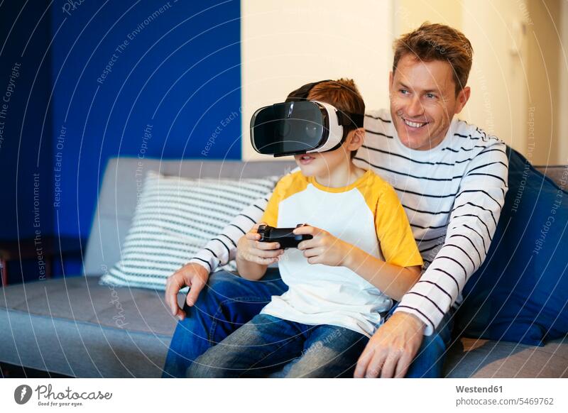 Junge mit VR-Brille spielt Videospiel mit seinem Vater zu Hause auf der Couch Sofa Couches Liege Sofas Videospiele Zuhause daheim spielen Virtuelle Realität