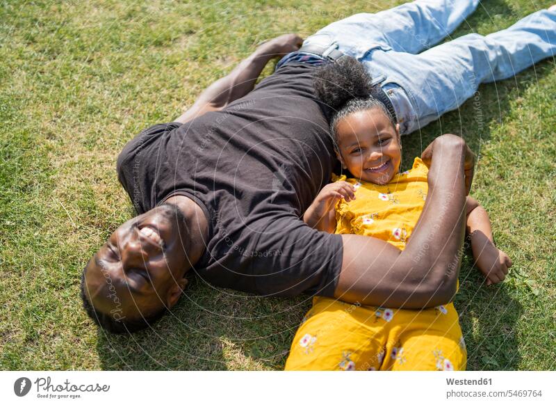 Glückliche Vater und Tochter liegen auf einer Wiese in einem Park entspannen relaxen knuddeln schmusen Jahreszeiten sommerlich Sommerzeit entspanntheit relaxt