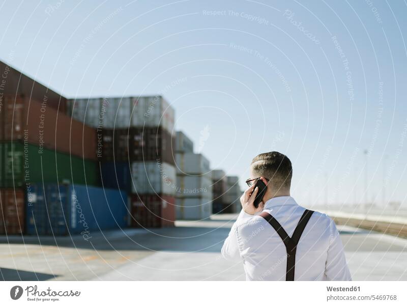 Rückansicht eines Managers, der vor Frachtcontainern auf einem Industriegelände mit einem Mobiltelefon spricht Spanien Sachverstand Sachkenntnis Kompetenz