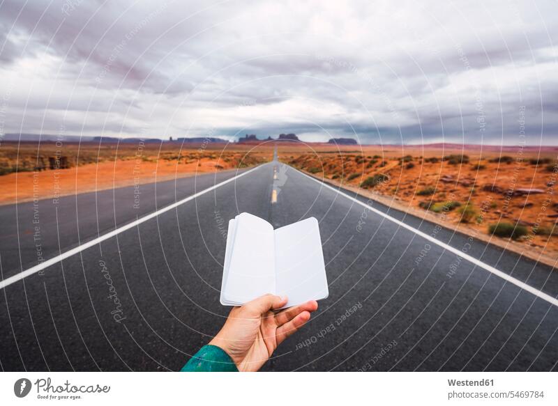 USA, Utah, Hand hält leeres Notizbuch über Straße zum Monument Valley Tagebuch Tagebücher Tagebuecher Hände junger Mann junge Männer Strassen Straßen Mensch