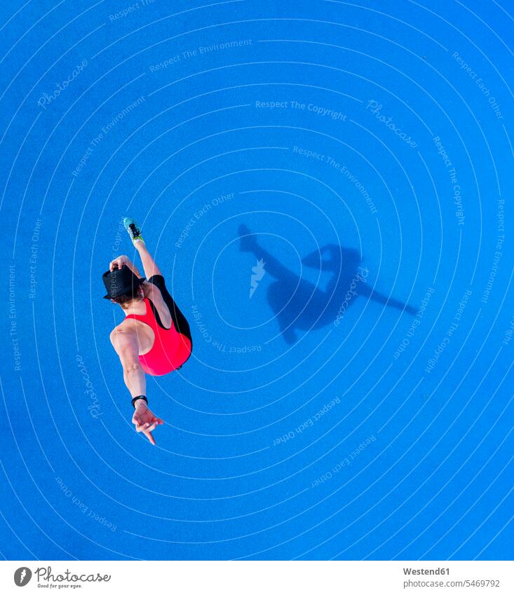 Springende junge Frau und ihr Schatten auf blauem Hintergrund, Draufsicht weiblich Frauen springen hüpfen blauer blaues Erwachsener erwachsen Mensch Menschen