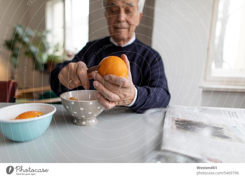 Älterer Mann schält zu Hause Orangen Schale Schalen Schälchen Schüsseln Zeitungen Tische sitzend sitzt früh Frühe Morgen daheim alltäglich Essen