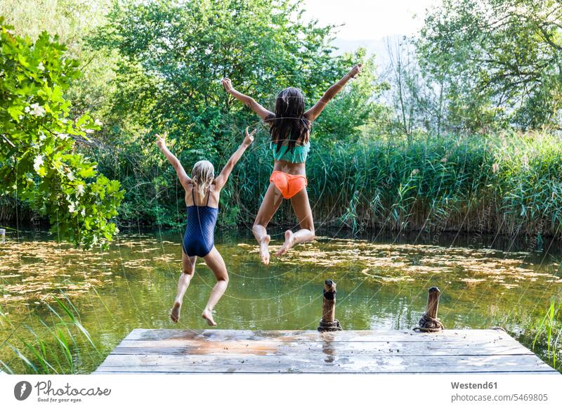 Zwei unbekümmerte Mädchen springen in den Teich Teiche weiblich hüpfen Unbeschwert Sorglos Freundinnen Gewässer Wasser Kind Kinder Kids Mensch Menschen Leute