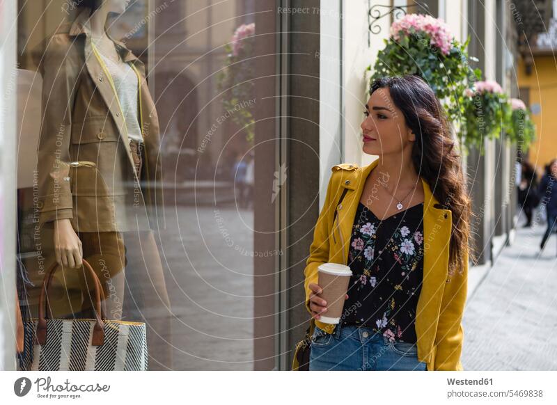 Porträt einer jungen Frau mit gelber Lederjacke, die beim Einkaufen eine Tasse Kaffee hält Coffee to go zum mitnehmen Shopping einkaufen shoppen unterwegs