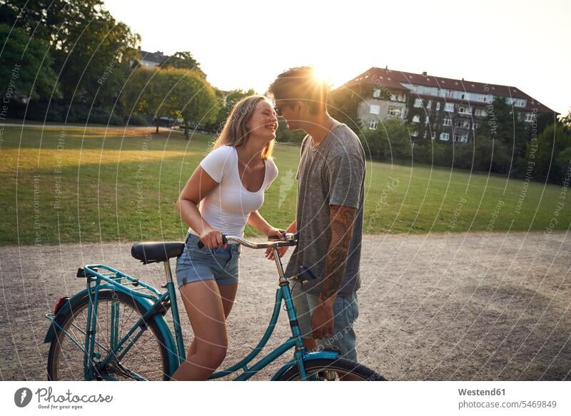 Junge Frau mit Fahrrad, küsst ihren Freund im Park frisch verliebt sich verlieben Junges Paar Junge Paare Parkanlagen Parks Erwachsenes Paar Erwachsene Paare