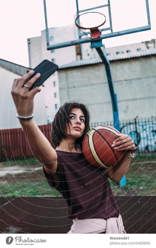 Junge Frau mit Basketball macht ein Selfie auf einem Platz im Freien Basketbaelle Basketbälle Selfies Sportplatz Sportplaetze Sportplätze weiblich Frauen